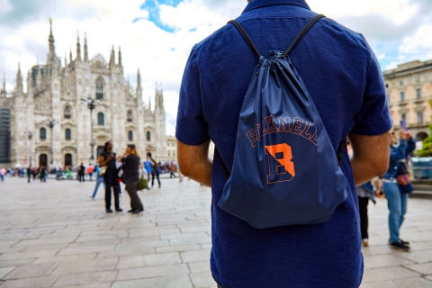 Bucknell student in a square in Milan. Student is facing away from the camera, wearing a Bucknell backpack. Cathedral in background. 