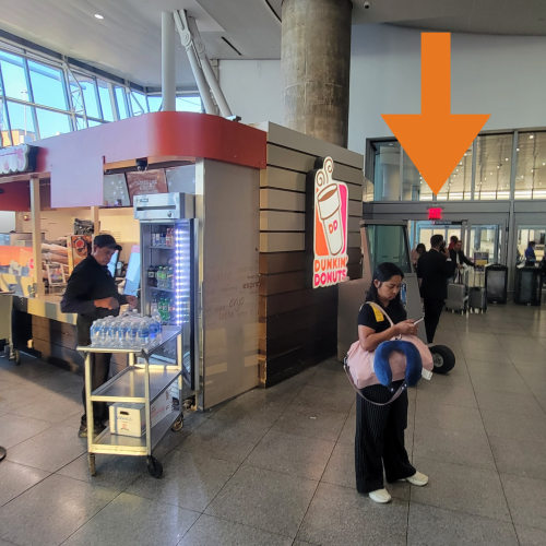 JFK shuttle pickup area. Dunkin' Donuts to the left and orange arrow pointing to exit door. 